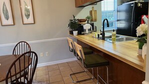 A kitchen with a wooden countertop, a sink, a refrigerator, and a dining area with a table and chairs. - Adorable Golf Course House in Tallahassee (Tallahassee)