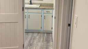 A doorway leading to a kitchen with light blue cabinets, a white countertop, and a window above the sink. - Four Bedroom house in Summerville GA (Summerville)