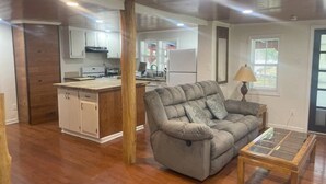 A living room with a sofa, a glass-top coffee table, and a kitchen area in the background. - Four Bedroom house in Summerville GA (Summerville)