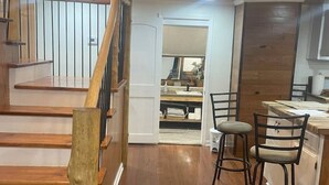 A modern kitchen with wooden flooring, a dining area with two bar stools, and a staircase with wooden railings. - Four Bedroom house in Summerville GA (Summerville)