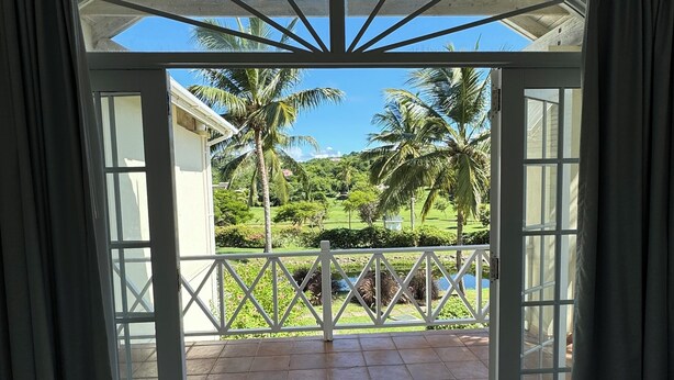 Une pièce dotée d’une grande porte vitrée donnant sur un balcon d’où l’on peut admirer des palmiers et un paysage verdoyant.