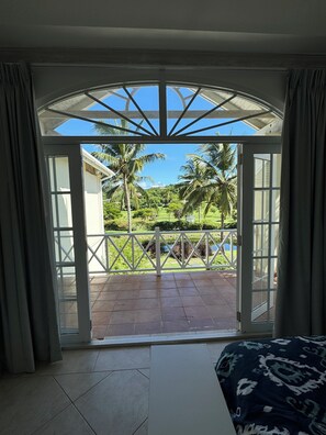 Quarto com uma grande porta de vidro que dá para uma varanda com vista para palmeiras e paisagem verde.
