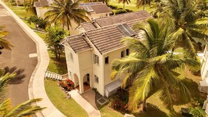 Une maison à deux étages, avec un toit recouvert de tuiles, entourée de palmiers et d’une pelouse bien entretenue.