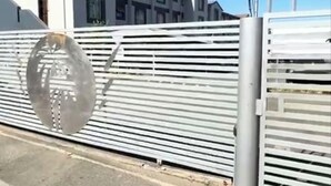 Ein durch einen Metallzaun abgegrenztes Areal mit einem Gebäude im Hintergrund.
