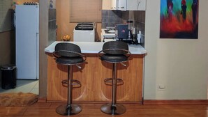 Eine kompakte Küche mit einer zentralen Kochinsel, zwei Barhocker, einem Kühlschrank und einer Kaffeemaschine.