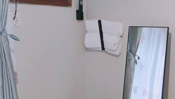 Una habitación con cama, un espejo de pie, un cubo de basura, aire acondicionado instalado en la pared y una ventana con persianas.