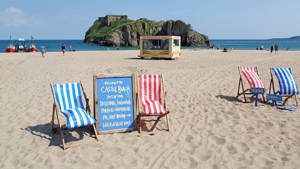 Cadeiras de praia com almofadas listradas, uma placa de aviso e um carrinho de comida para a praia.