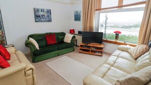 Uma sala de estar com um sofá verde, um sofá bege e uma televisão de tela plana em um suporte de madeira.