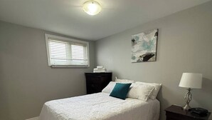 A bedroom with a bed, a nightstand, a window with blinds, and a ceiling light. - Cozy 2BR Loft Fast WiFi Parking (St. John's)