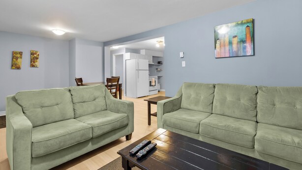 A living room with two green sofas, a coffee table, and a painting on the wall. - Cozy 2BR Loft Fast WiFi Parking (St. John's)