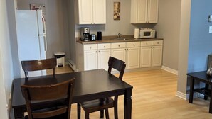 A dining area with a dark wooden table and chairs, a kitchen with white cabinets and appliances, and a light-colored wooden floor. - Cozy 2BR Loft Fast WiFi Parking (St. John's)