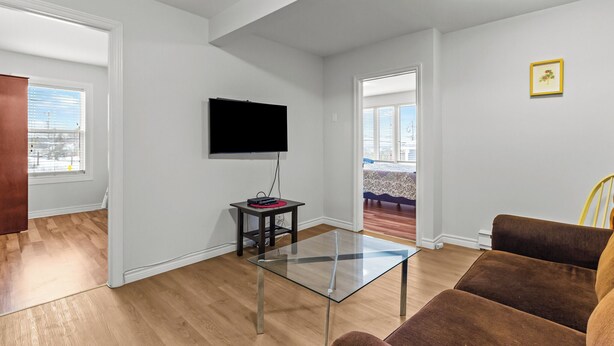 A modern living room with a glass coffee table, a brown sofa, and a flat-screen TV mounted on the wall. - Bright 2BR Loft WiFi Parking (St. John's)