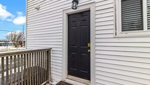 A white house with a black front door, a small porch, and a window with blinds. - Bright 2BR Loft WiFi Parking (St. John's)