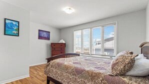 A bedroom with a wooden floor, a bed with a patterned bedspread, a dresser, and two wall-mounted paintings. - Bright 2BR Loft WiFi Parking (St. John's)