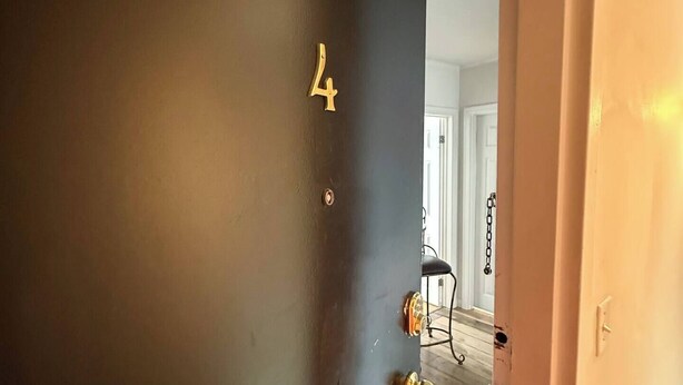 Une porte sombre, portant le numéro 4, avec une poignée de porte en laiton et un verrou à chaîne.
