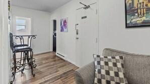 Un salon comprenant un canapé, un coussin décoratif à motifs, une chaise en métal et une porte sur laquelle est accrochée une peinture.
