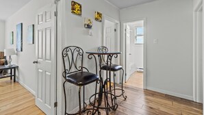 Un couloir avec deux chaises en métal noir et une petite table, des murs blancs et un plancher en bois franc.