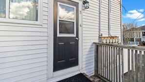 Une maison blanche avec une porte d’entrée noire, une fenêtre et une clôture en bois.