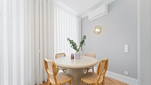A dining area with a round table, four wicker chairs, a vase with greenery, and a wall-mounted air conditioner.