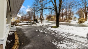 En bostadsgata med snötäckt mark, lövträ utan löv och hus.