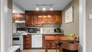 A kitchen with wooden cabinets, a stove, microwave, dishwasher, and a dining area with a table and chairs. - Midstream Manor 1BR Parking WiFi (St. John's)
