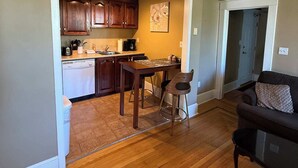 A spacious living area with hardwood flooring, a dining table with chairs, a sofa, and a kitchen with wooden cabinets and a coffee maker. - Midstream Manor 1BR Parking WiFi (St. John's)