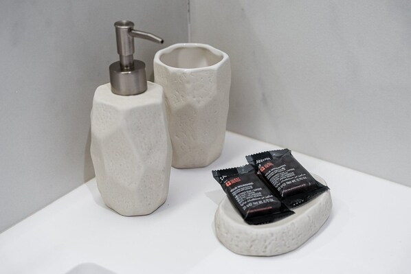 Un baño con dispensador de jabón y una taza sobre una superficie blanca.