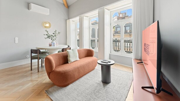A modern living room with a sofa, a small table, a TV, and a window with a view of buildings.