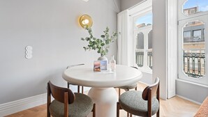 A dining area with a round table, two chairs, a potted plant, and a wall-mounted light fixture.