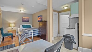 A compact room with a bed, a desk, a chair, a dresser, a trash bin, and a kitchenette. - Chic Midstream Studio WiFi Parking (St. John's)