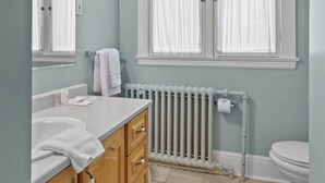 A bathroom with a white sink, wooden cabinets, a radiator, and a toilet. - Chic Midstream Studio WiFi Parking (St. John's)