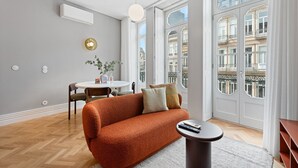 Ein modernes Wohnzimmer mit einer Couch, einem Esstisch und Blick auf die Stadt durch große Fenster.