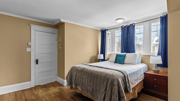 Une chambre à coucher avec un lit, des tables de chevet, une fenêtre avec des rideaux et une porte.