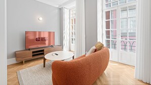 Ein modernes Wohnzimmer mit Flachbildfernseher, rundem Couchtisch und einer bequemen, orangefarbenen Couch.