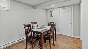 A dining area with a rectangular table surrounded by six wooden chairs, a white door, and a framed picture on the wall. - Stylish 2BR WiFi Parking MUN Walk (St. John's)