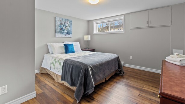 A bedroom with a bed, a nightstand, a lamp, a window, and a wardrobe. - Stylish 2BR WiFi Parking MUN Walk (St. John's)