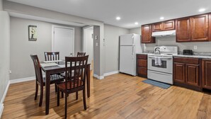 A kitchen with wooden cabinets, a refrigerator, stove, and a dining area with a table and chairs. - Stylish 2BR WiFi Parking MUN Walk (St. John's)