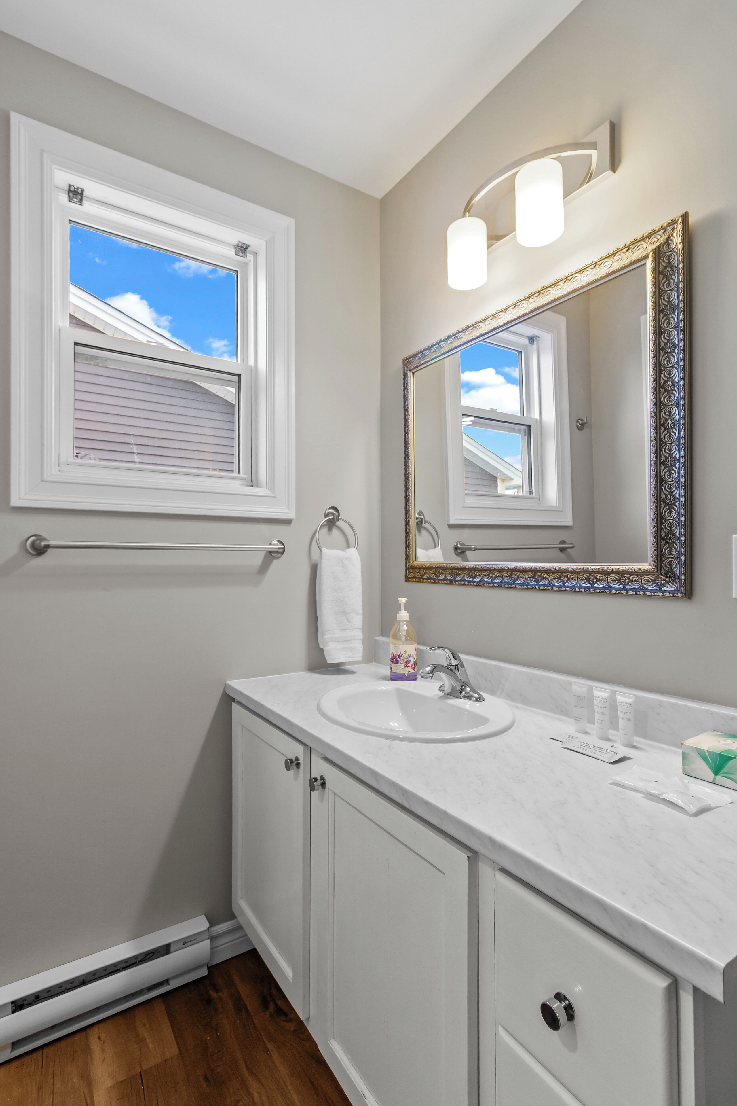 Un baño con tocador blanco, un espejo grande con marco decorativo, un perchero y una ventana con persianas.