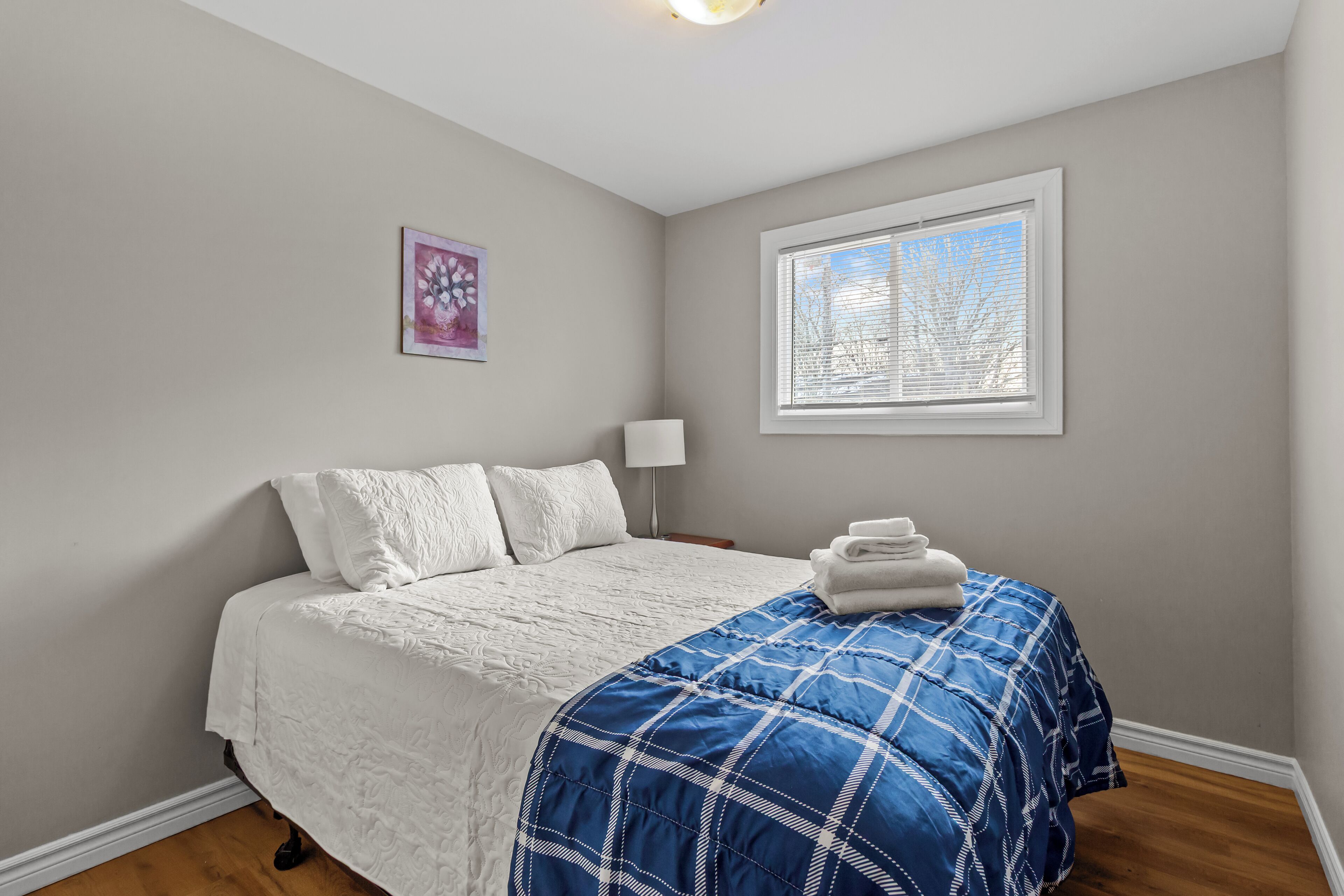 Une chambre à coucher avec un lit, une fenêtre, une lampe et un tableau au mur.