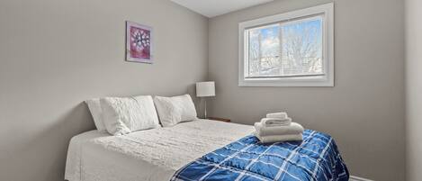 Une chambre à coucher avec un lit, une fenêtre, une lampe et un tableau au mur.