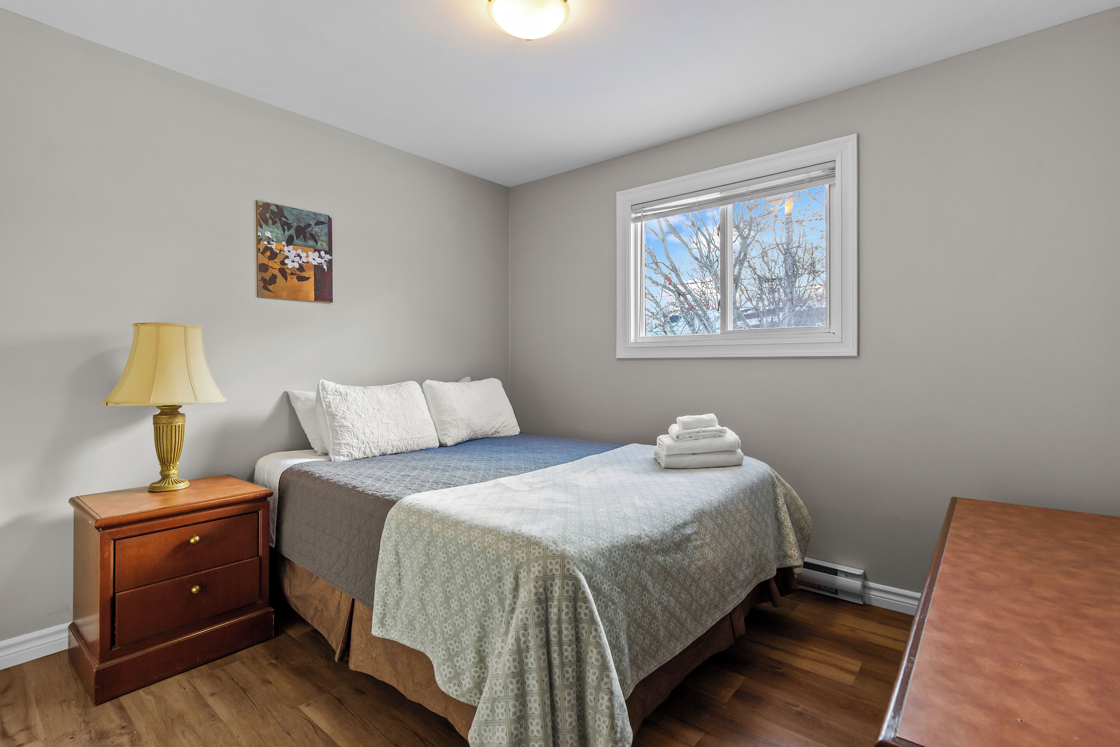A bedroom with a bed, bedside table, lamp, and a window.
