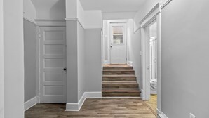 Un couloir doté d’un plancher en bois, de murs blancs et d’une porte donnant sur un escalier.