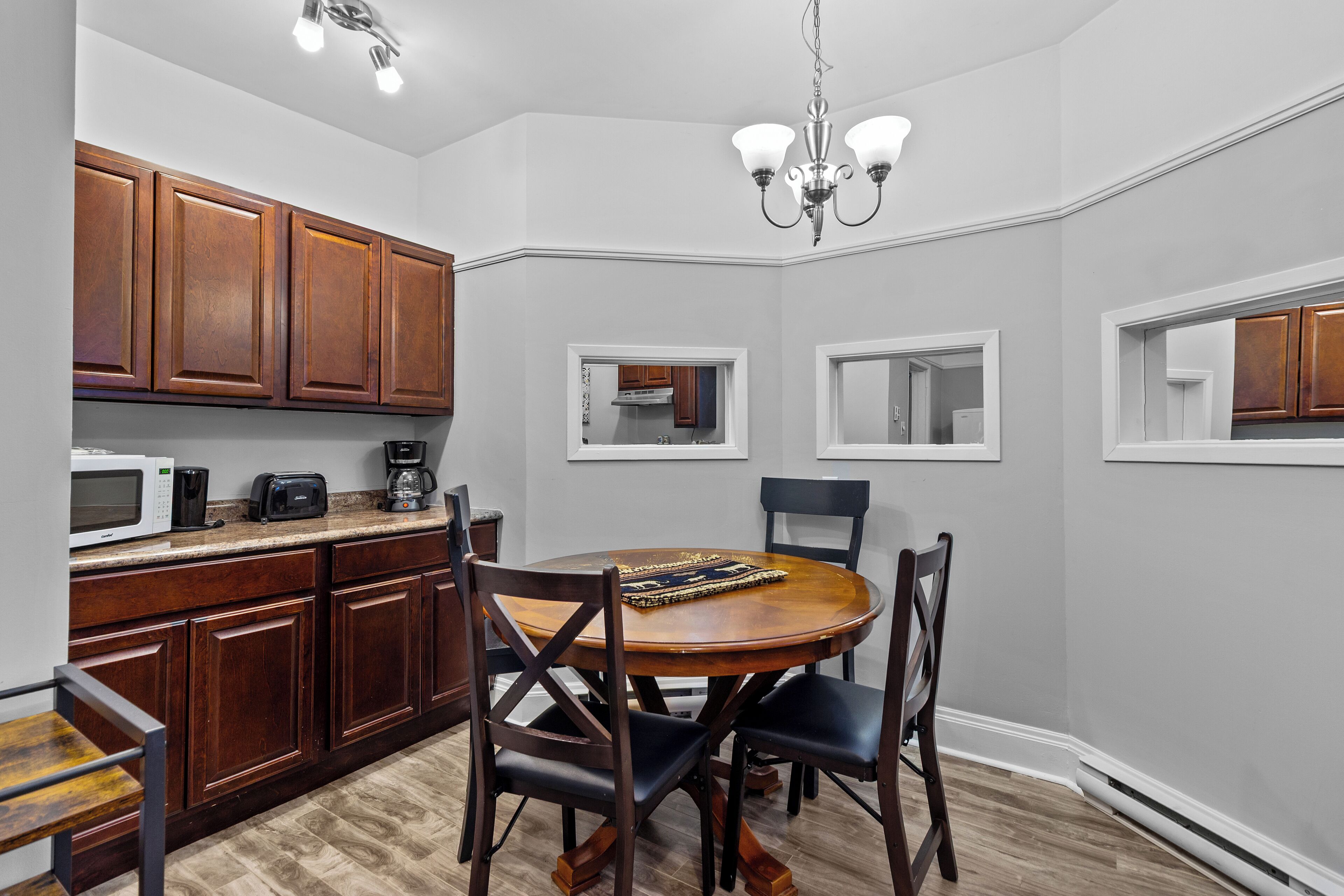 A kitchen with wooden cabinets, a microwave, a toaster, and a coffee maker on the countertop. There is a dining table with chairs and a chandelier above.