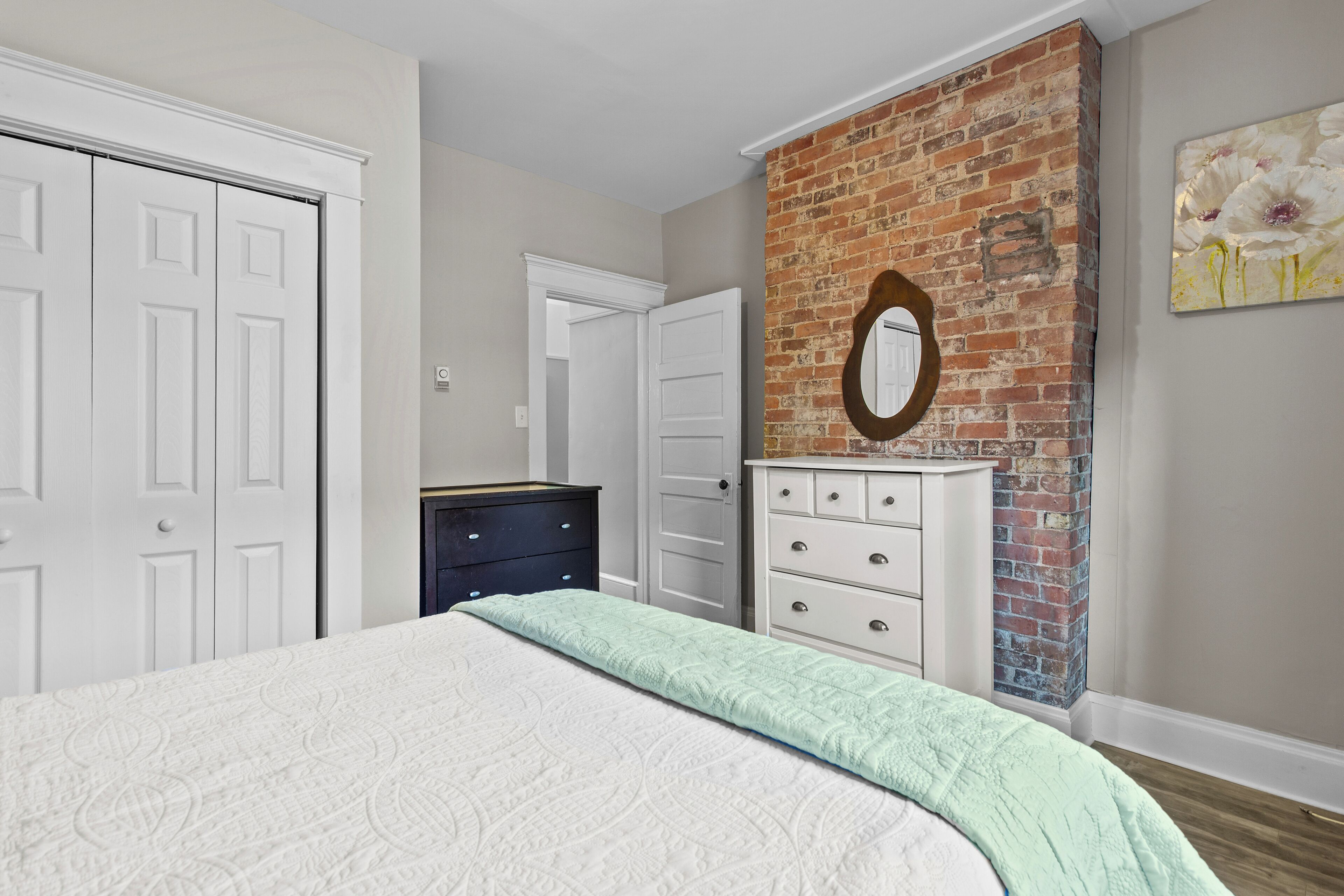 Une chambre à coucher avec un lit, une commode, un miroir et un mur décoratif en briques.