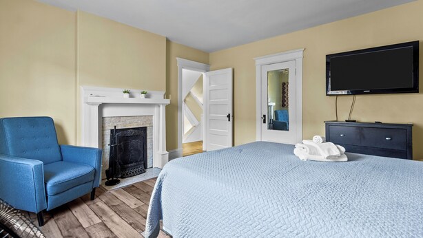 A bedroom with a bed, a blue armchair, a fireplace, a television, and a nightstand.