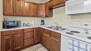 A kitchen with wooden cabinets, a microwave, a coffee maker, a sink, and a stove.