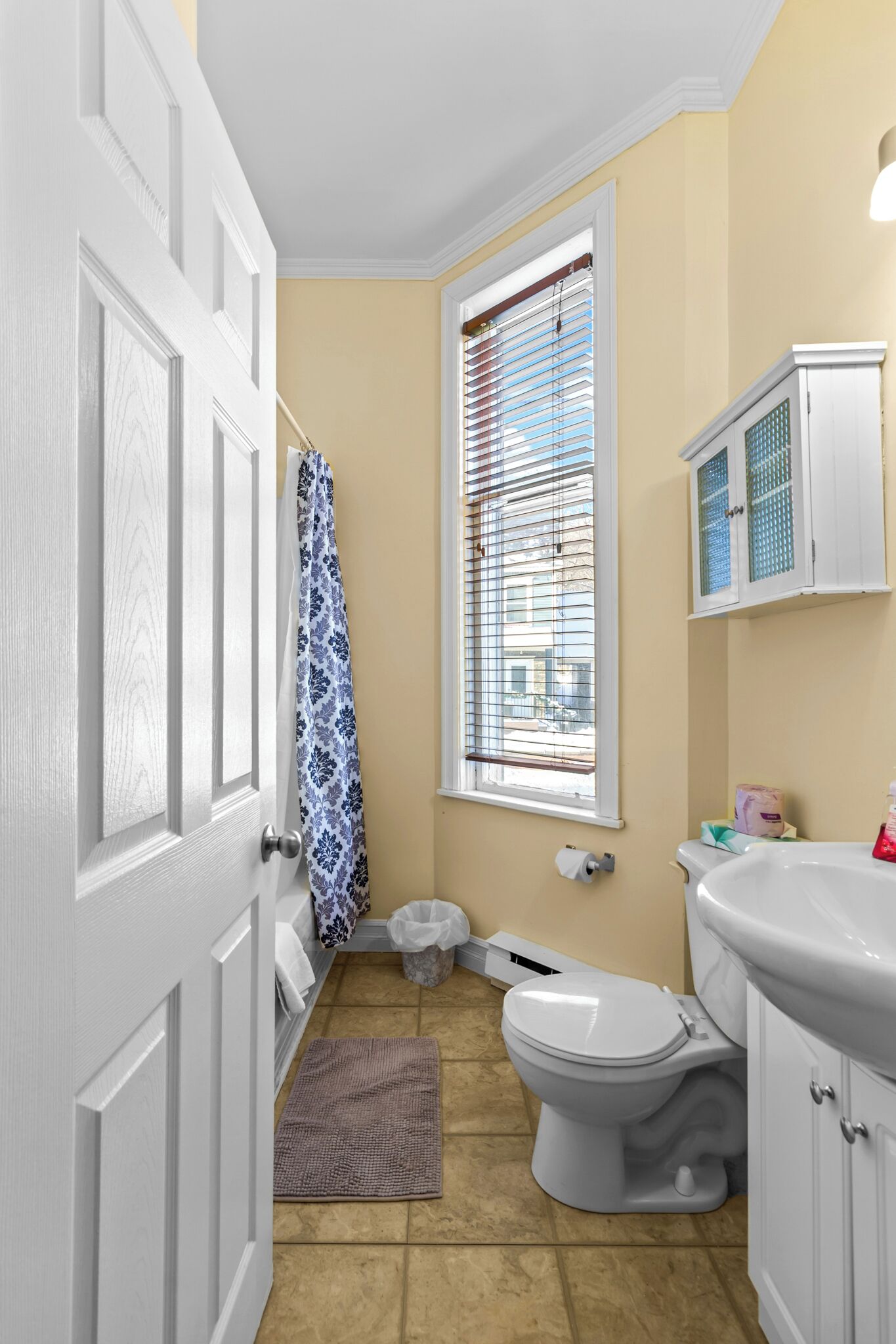 A small bathroom with a toilet, sink, and window with blinds.