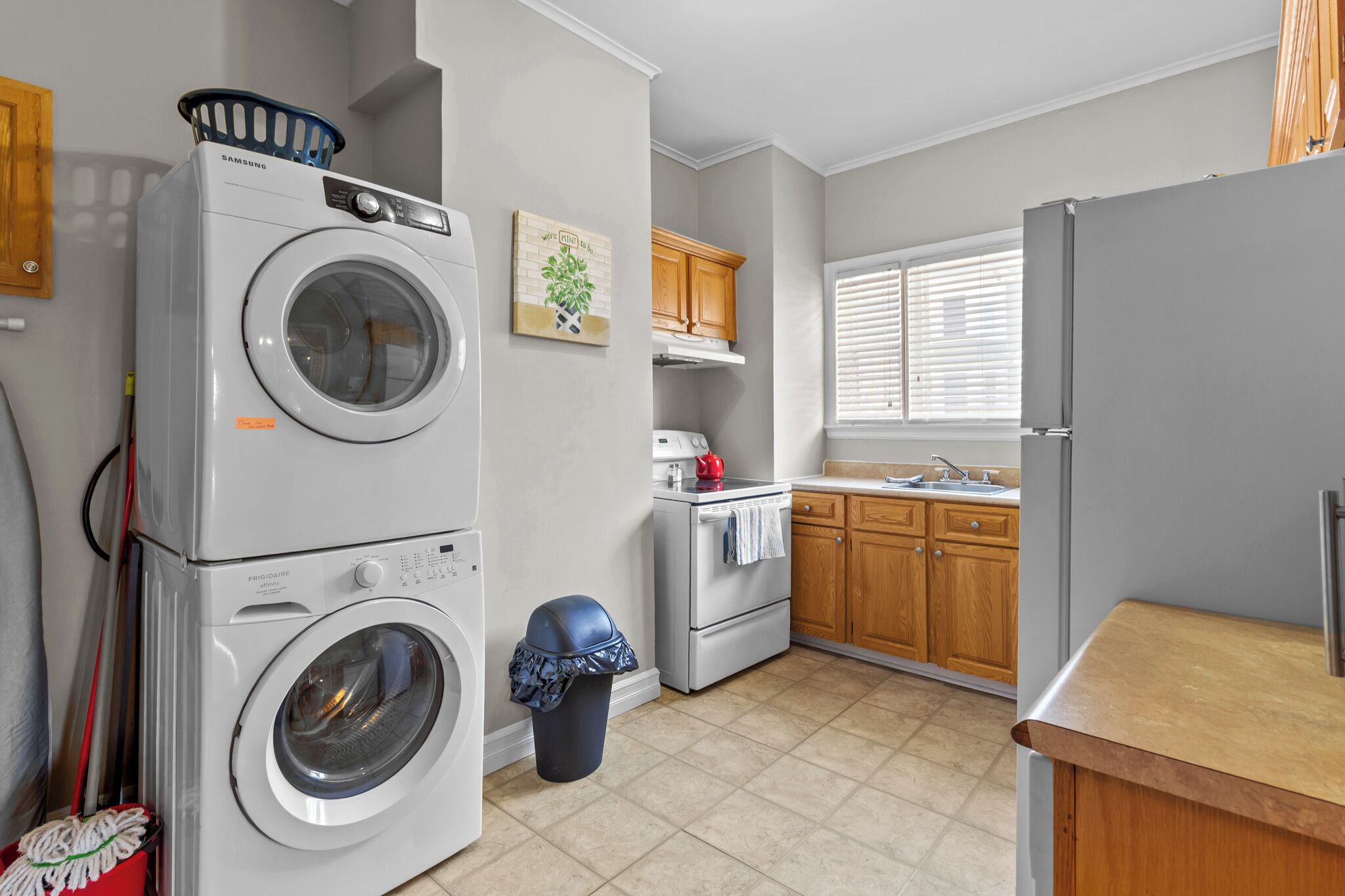 A laundry area with stacked washers and dryers, a small trash bin, a stove, and wooden cabinets.