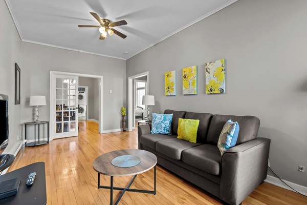 Spacious, sun-filled living room featuring hardwood floors, a comfortable full-sized sofa, and vibrant decor. Perfect for relaxing after a day of exploring.