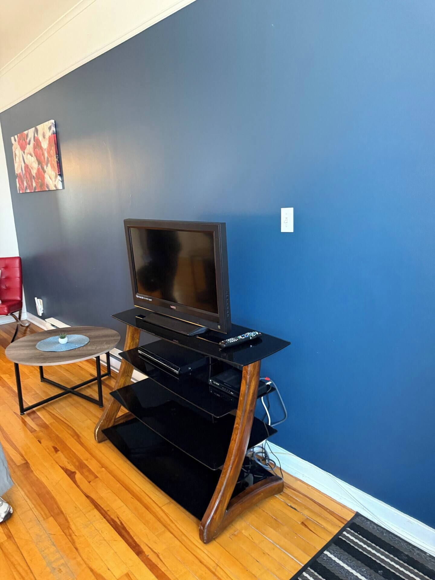 A living room with a TV on a black entertainment unit, a small round table with a plant, and a red chair.